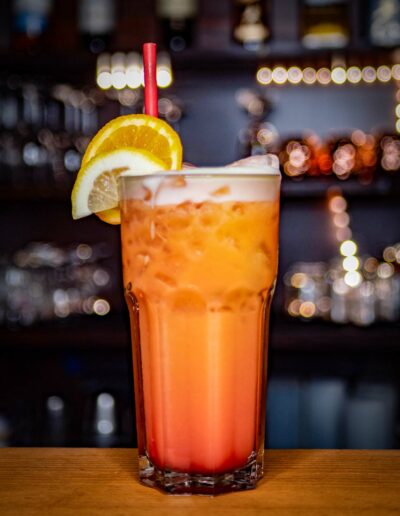Orange-roter Cocktail mit Zitronen- und Orangenscheibe auf einer Theke