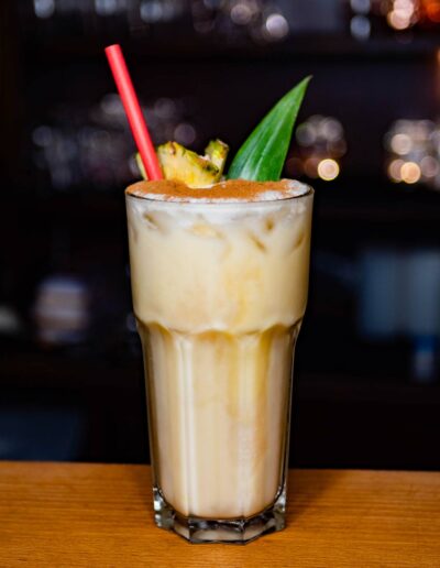 Heller Cocktail mit Ananasscheibe, Zimt und Strohhalm