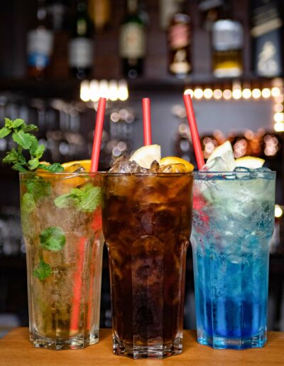 Drei Cocktails in hohen Gläsern in hell, dunkel und blau mit Eiswürfeln
