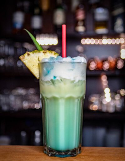 Hellblauer Cocktail mit Ananasscheibe und Strohhalm